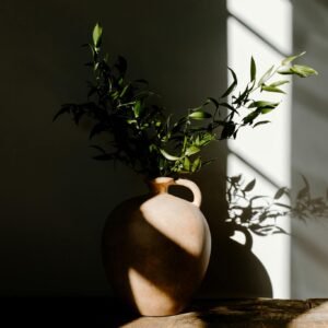 A minimalist-style ceramic vase adorned with lush green foliage casting elegant shadows.