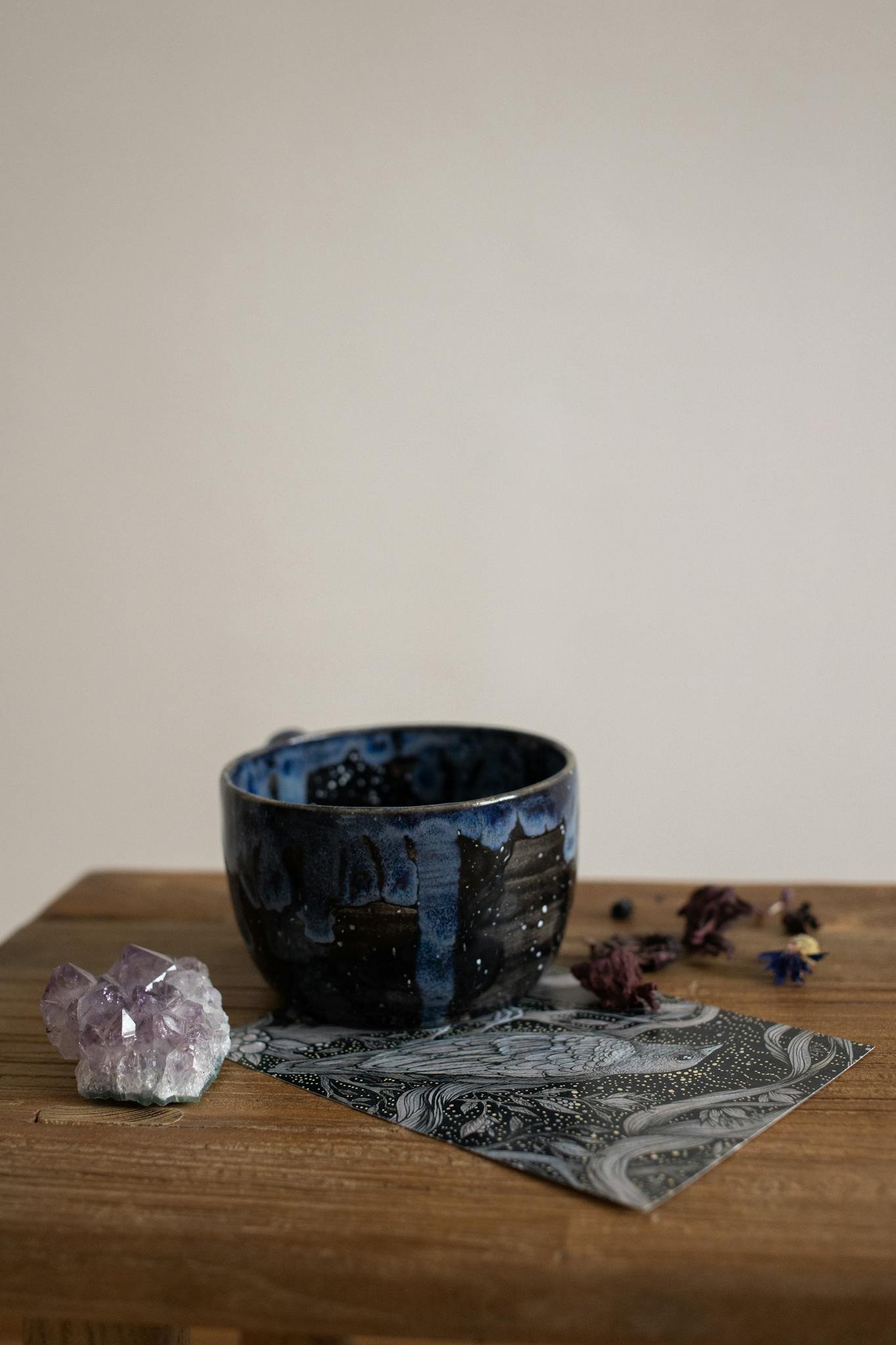 Elegant still life of a blue ceramic cup with an amethyst crystal and patterned paper on a wooden table.